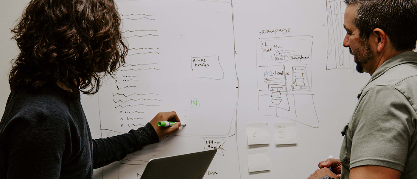 Two people collaborate at a whiteboard filled with sketches and notes