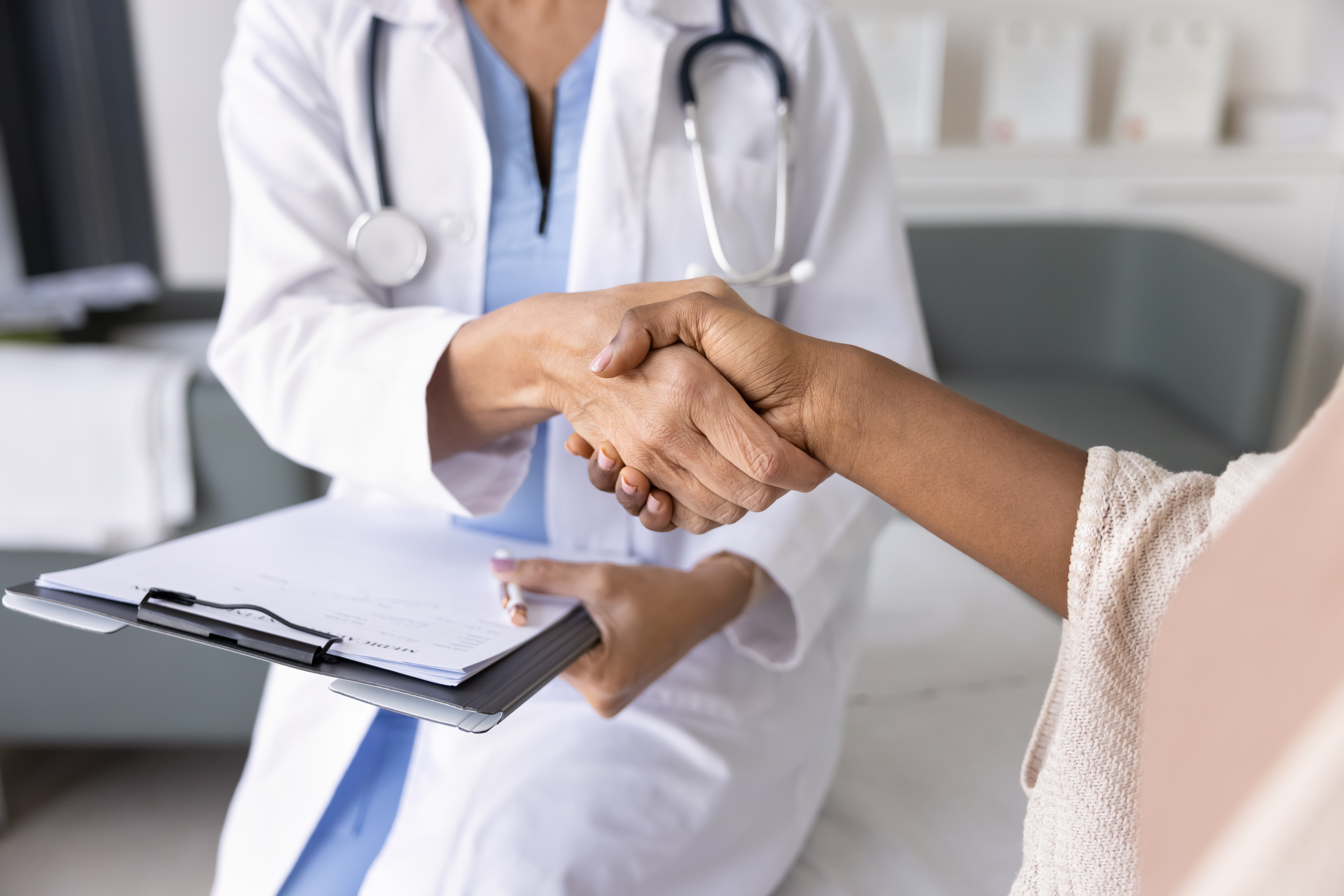 Female doctor holding clipboard and shaking hands with patient; Untitled photo of a doctor in a white coat shakes hands with a patient while holding a clipboard. Image credit: By fizkes, Adobe Stock.;  Photo of a doctor in a white coat shakes hands with a patient while holding a clipboard. Image credit: By fizkes, Adobe Stock.