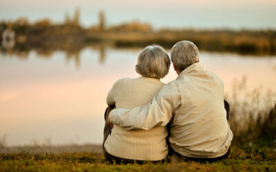 Older couple seated on lakeside with man's arm around woman